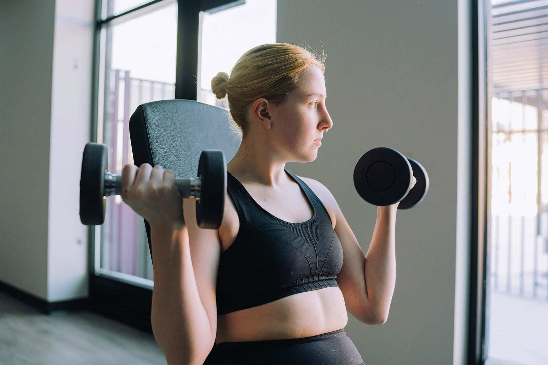 Pregnant woman lifting dumbbells in gym.