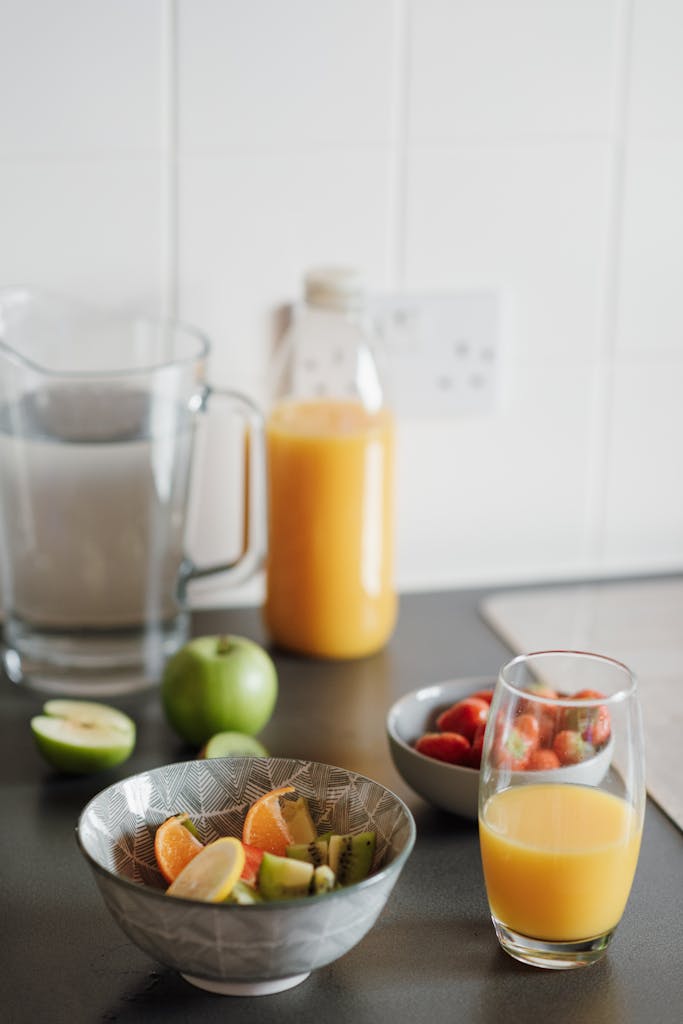 High angle of glass of fresh juice and bowls with fruit salad and small bowl with strawberries